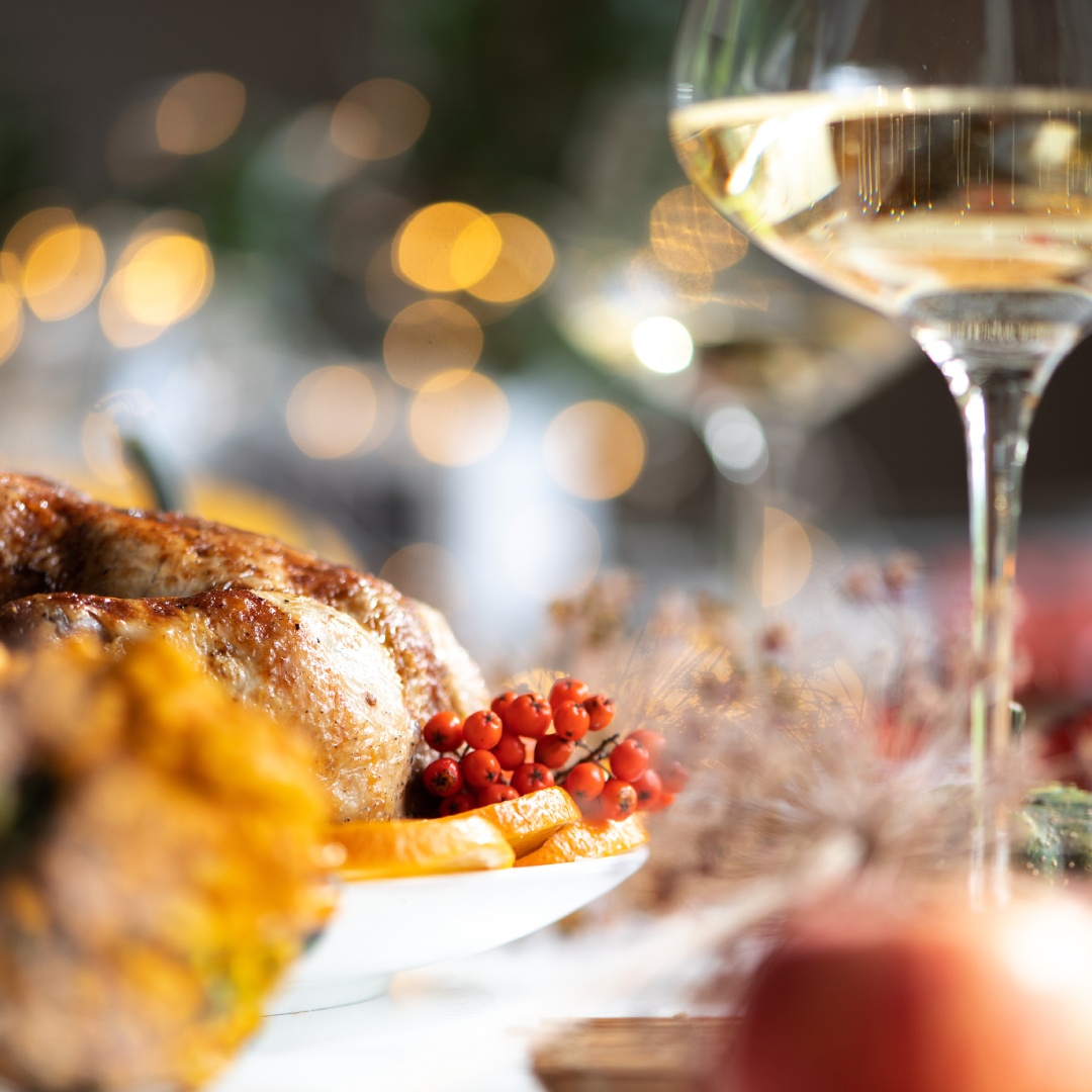 Close-up of a Thanksgiving dinner table with a roasted turkey and a glass of sparkling white wine.